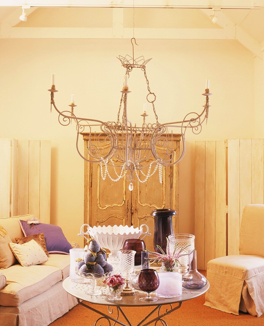Sitzecke mit reich gedecktem Glastisch und filigranem Kronleuchter vor opulentem Schrank und einfachen Paravents