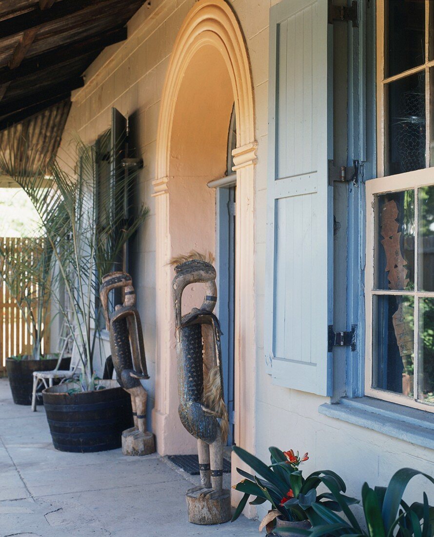 Überdachter Eingangsbereich mit Rundbogentür und Ethnoskulpturen