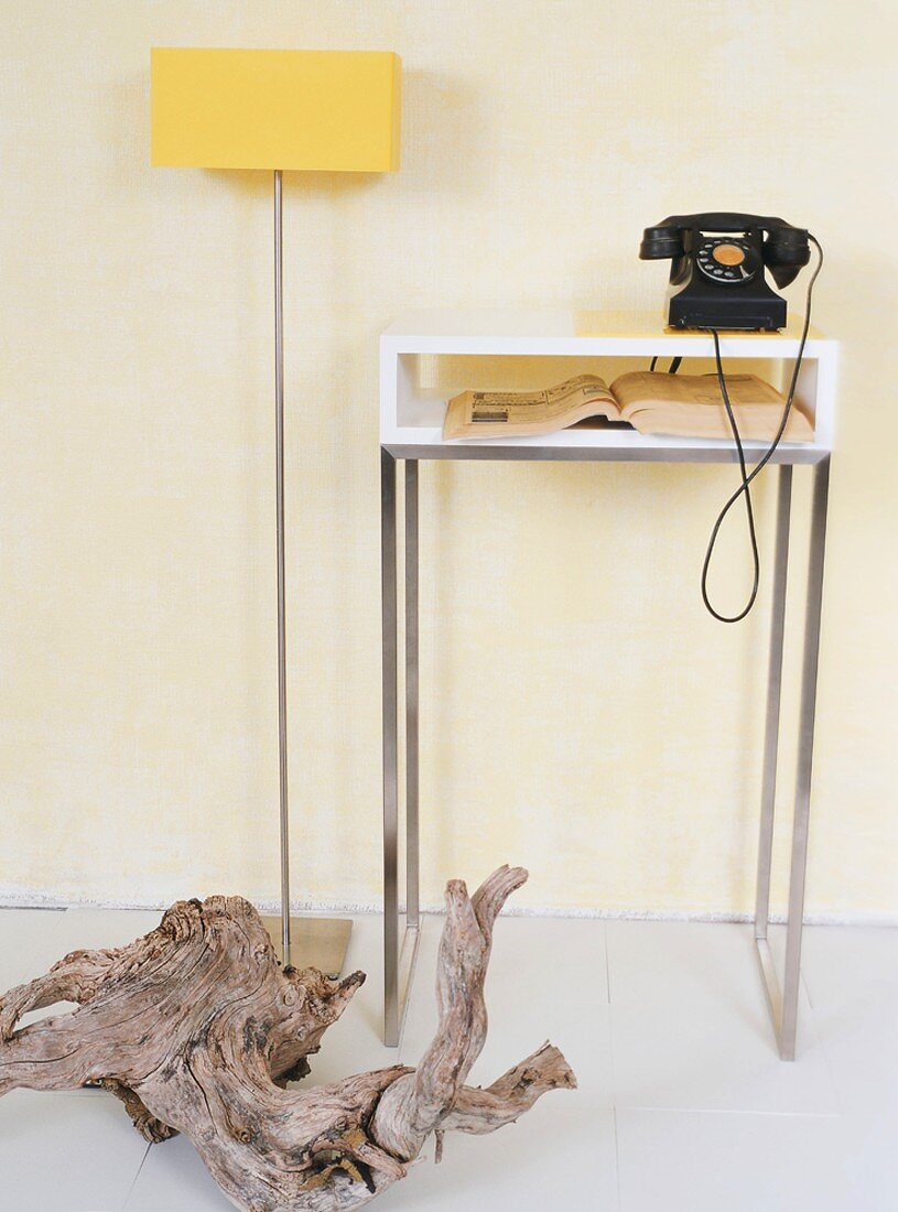 Moderne Stehlampe und Telefontisch mit altem Wählscheibentelefon und einem Stück Treibholz