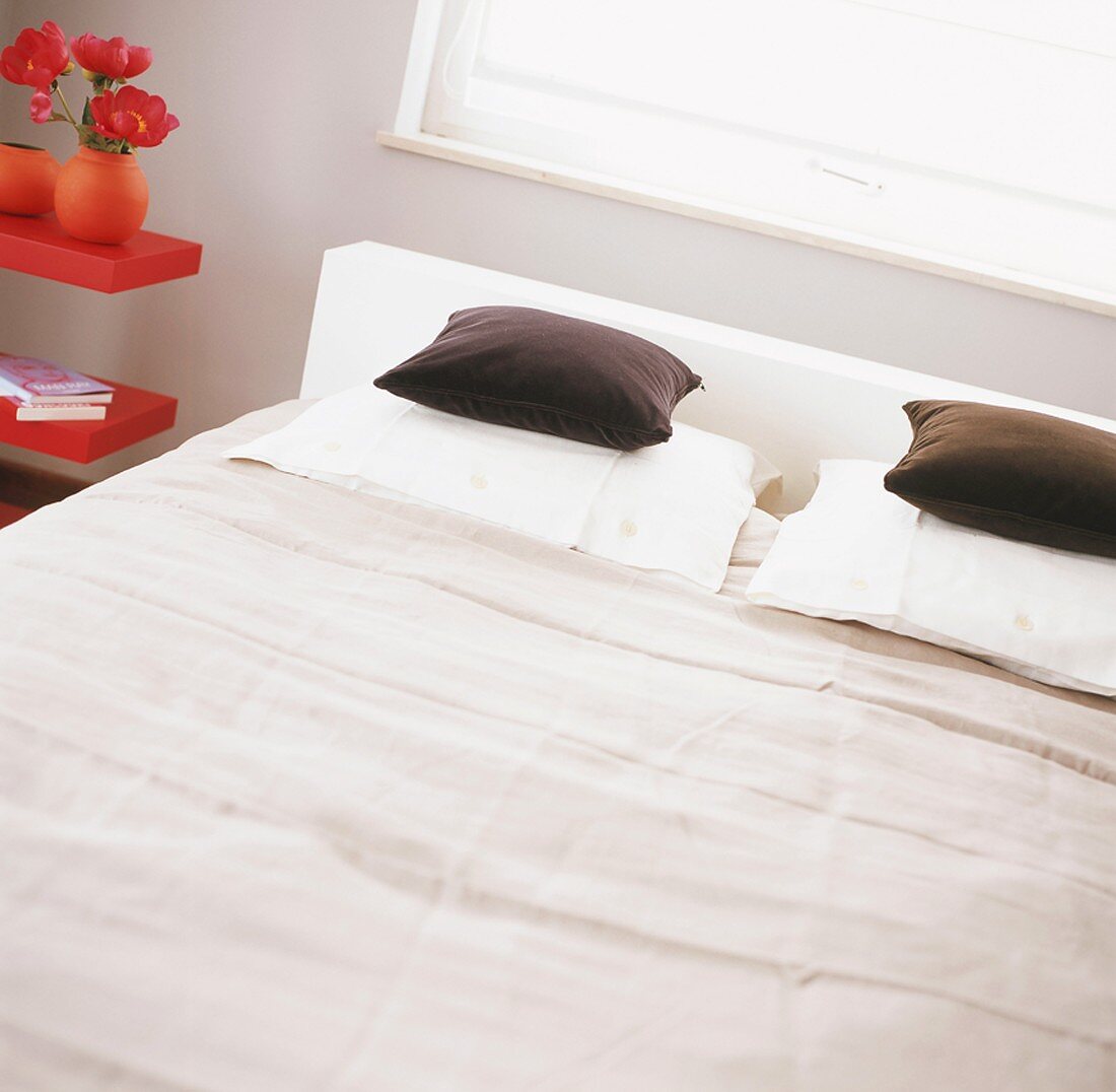Ein gemachtes Bett mit rotem Beistelltisch und roten Blumenvasen