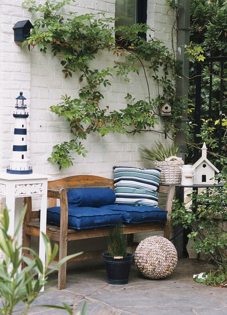Holzbank mit Kissen im Garten mit Leuchtturm, Vogelhäuschen