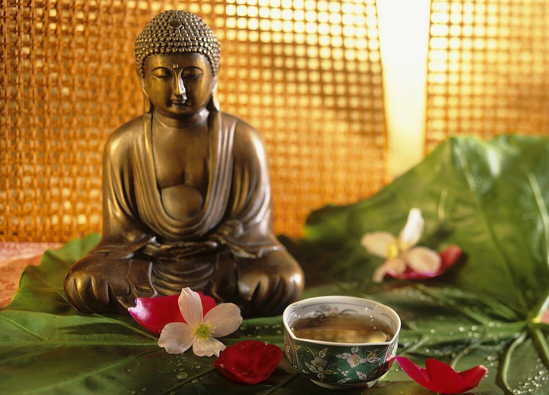 Eine Schale Pu-Erh-Tee, Blütendeko & Buddhafigur