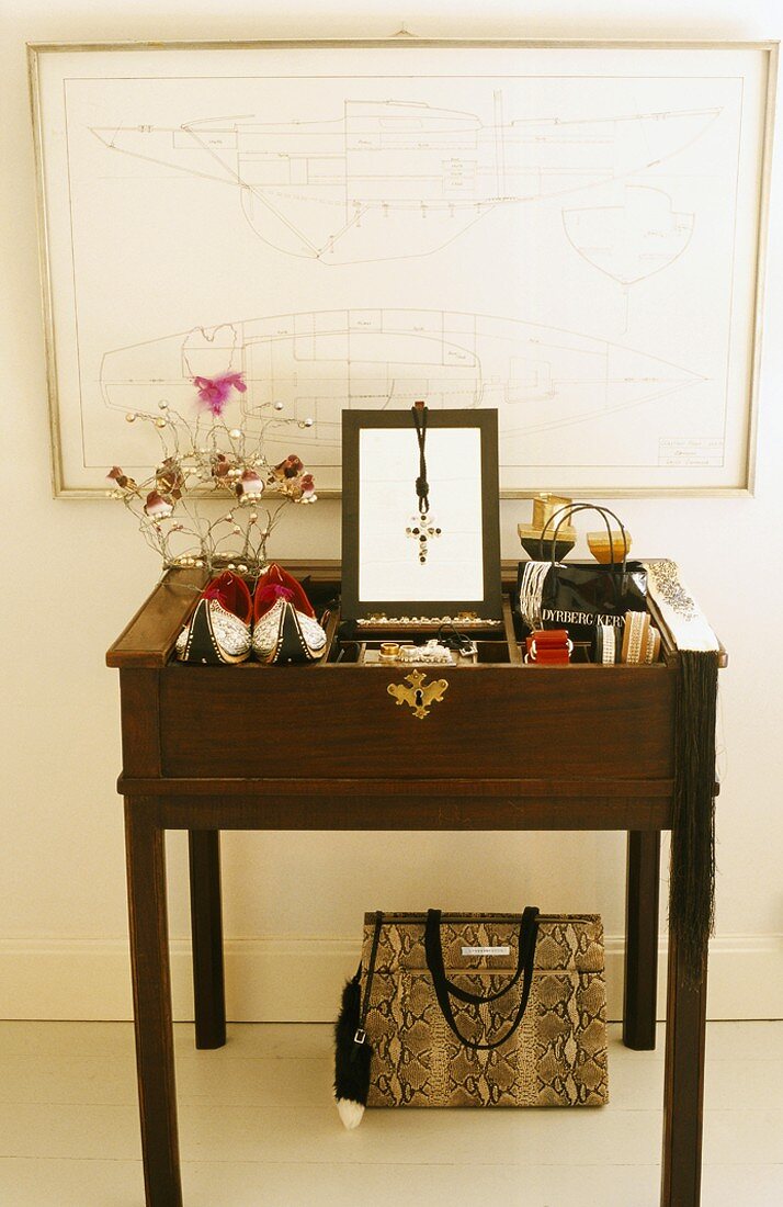 Ein Zimmerausschnitt mit antikem, bunt dekoriertem Sekretär, Bilderrahmen und Schlangenlederhandtasche