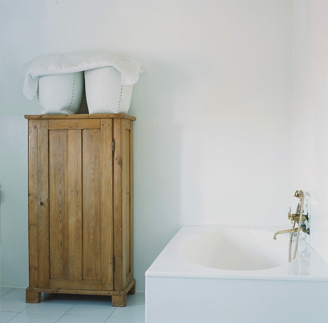 Ein antiker Holzschrank neben einer schlichten Badewanne