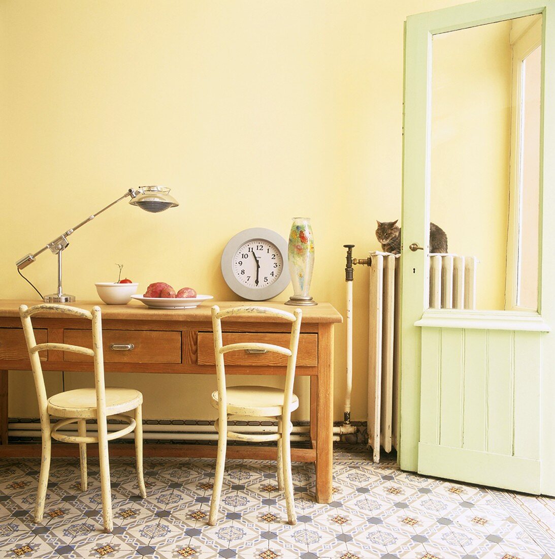 Alter Küchentisch und Vintagestühle vor einer gelben Wand