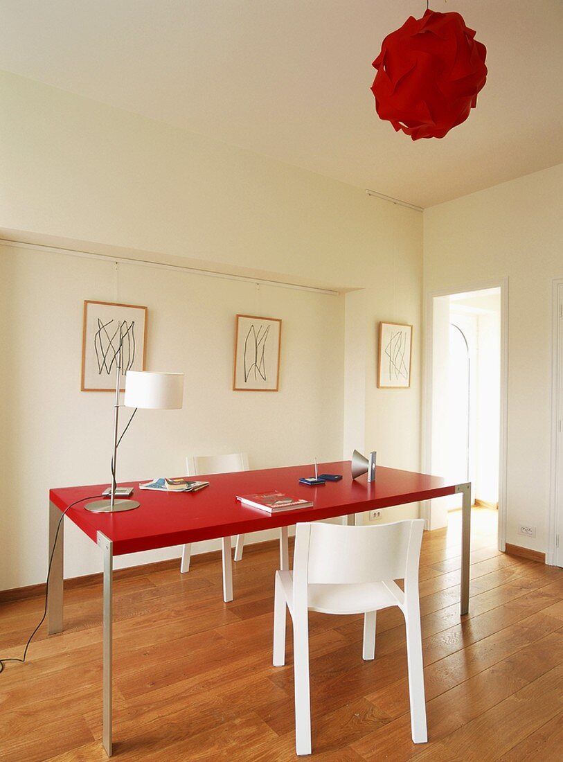 Der Tisch und die Deckenleuchte in sattem Rot durchbrechen das strenge Weiß des modern gestalteten Raumes