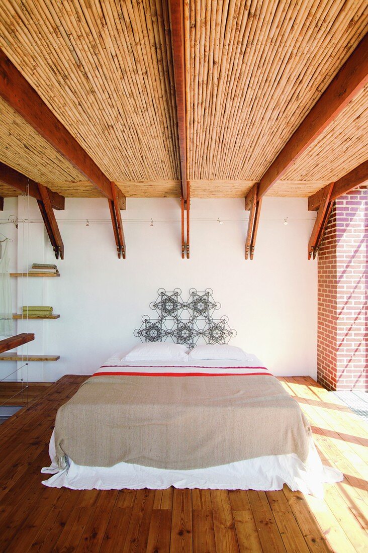 Eine ausgefallene Holzbalkendecke ist der Blickfang des spartanisch eingerichteten Schlafzimmers