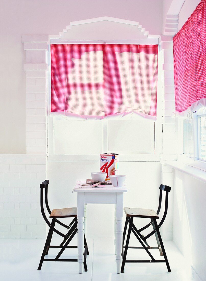 Schmaler Vintagetisch und Designerstühle bilden die Essecke des mit pinken Gardinen akzentuierten Raumes