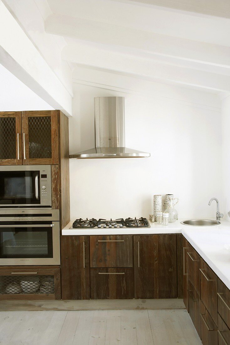 Eine interessante Mischung aus rustikalen Holzfronten und modernen Einbaugeräten in der Küche mit Dachschräge