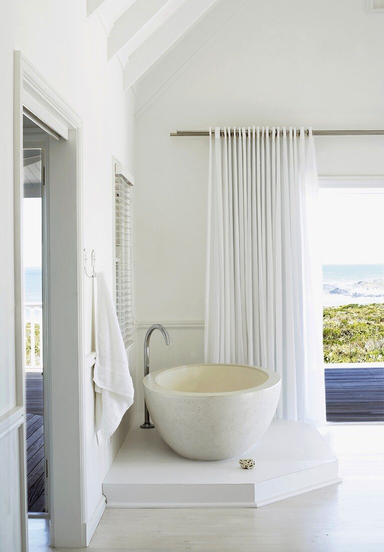Eine minimalistische Badewanne in einem Badezimmer mit schöner Aussicht über die Terrasse aufs Meer