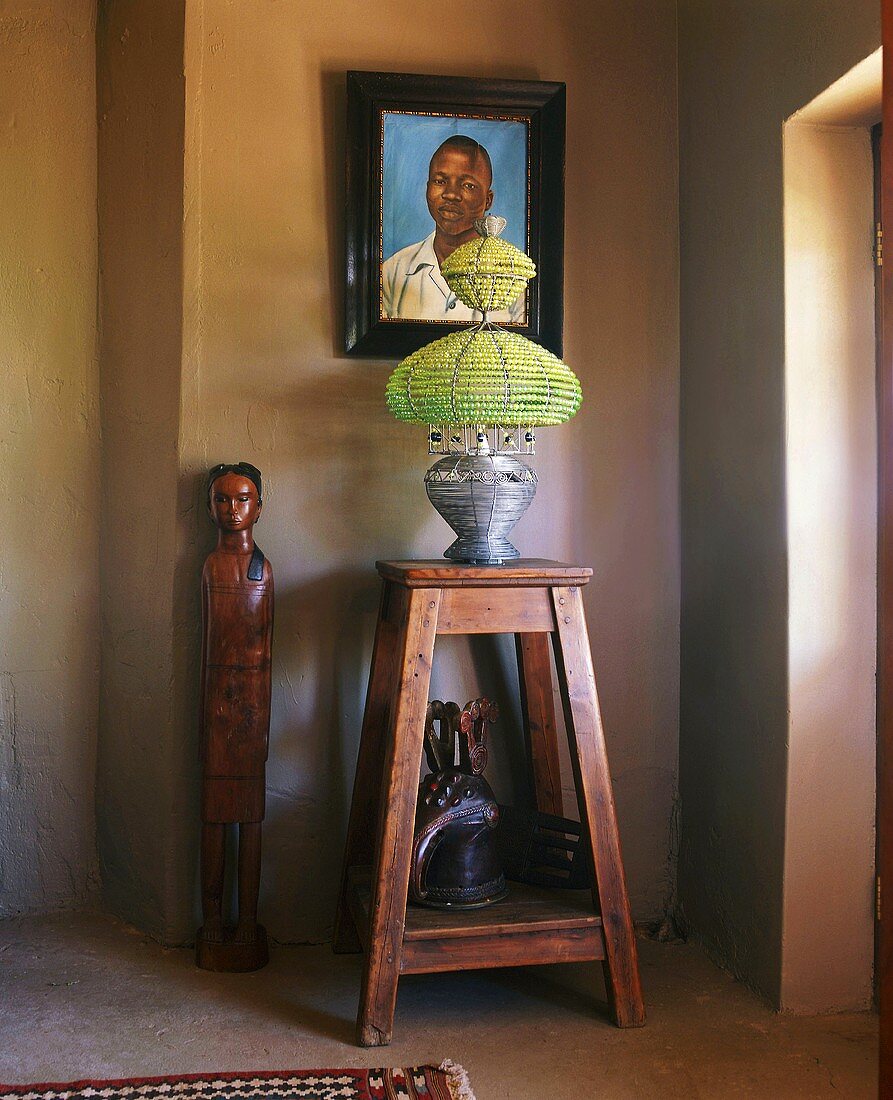 Afrikanische Holzskulpturen und eine Tischleuchte im Ethnostil auf einem einfachen Beistelltisch aus Holz