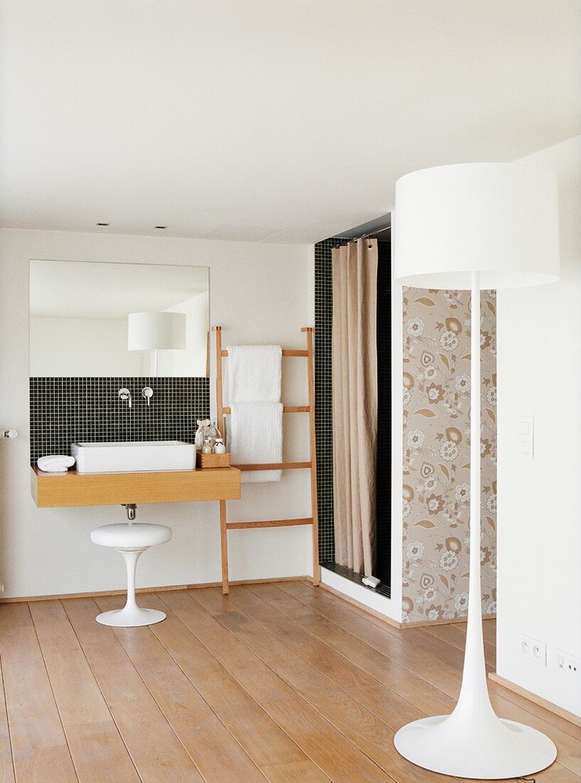 Schwarze Mosaikfliesen an Dusche und Waschtisch sowie Tapete und Stehleuchte im Retrostil bilden die Details des schlichten Badezimmers mit Holzboden