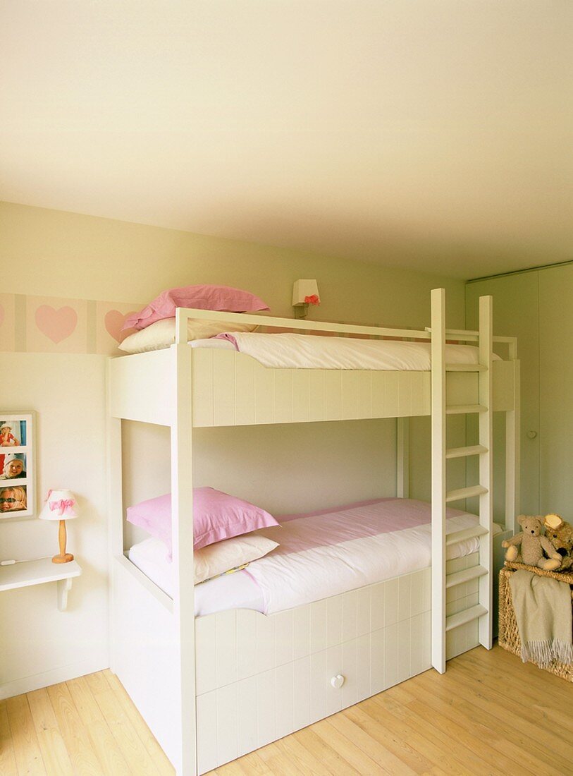 Ein einfaches, weisses Stockbett in einem aufgeräumten Kinderzimmer mit rosa Details