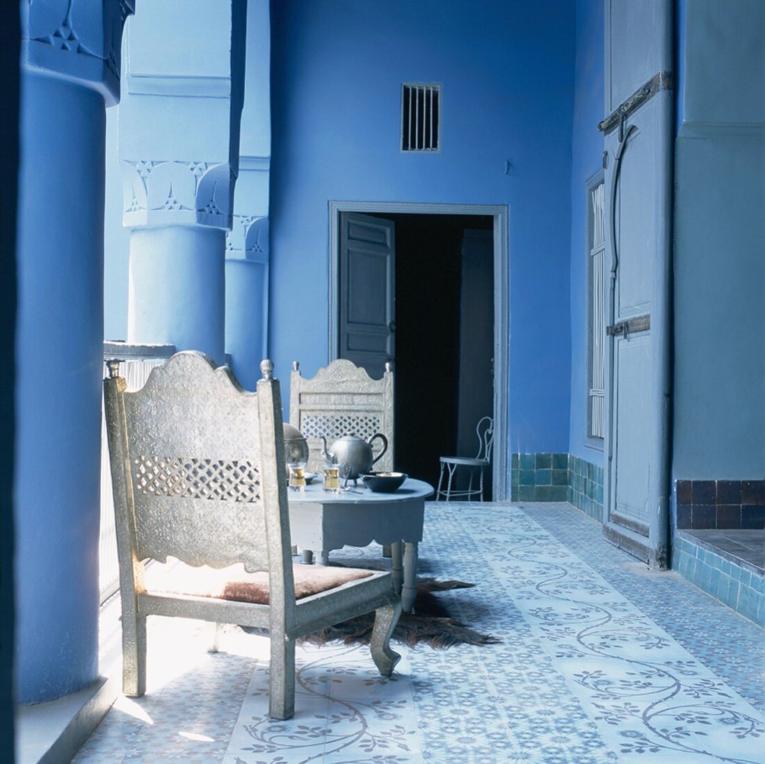Weissgold gestrichene, niedrige Holzstühle und ein gedeckter Kaffeetisch im blauen Arkadengang eines orientalischen Wohnhauses