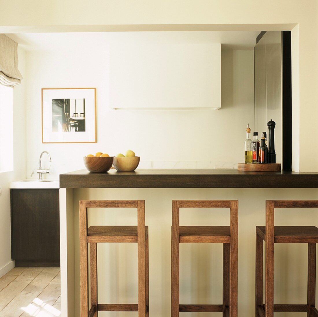 Eine Frühstückstheke mit minimalistischen Barhockern grenzt die moderne Küche vom Wohnbereich ab