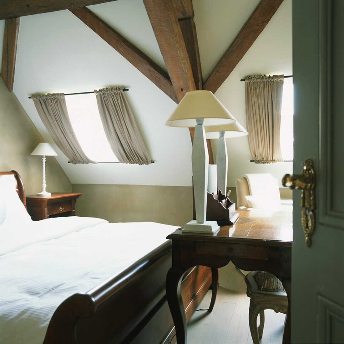 Elegante Antikmöbel in einem kleinen Dachgeschossschlafzimmer mit Holzbalkendecke