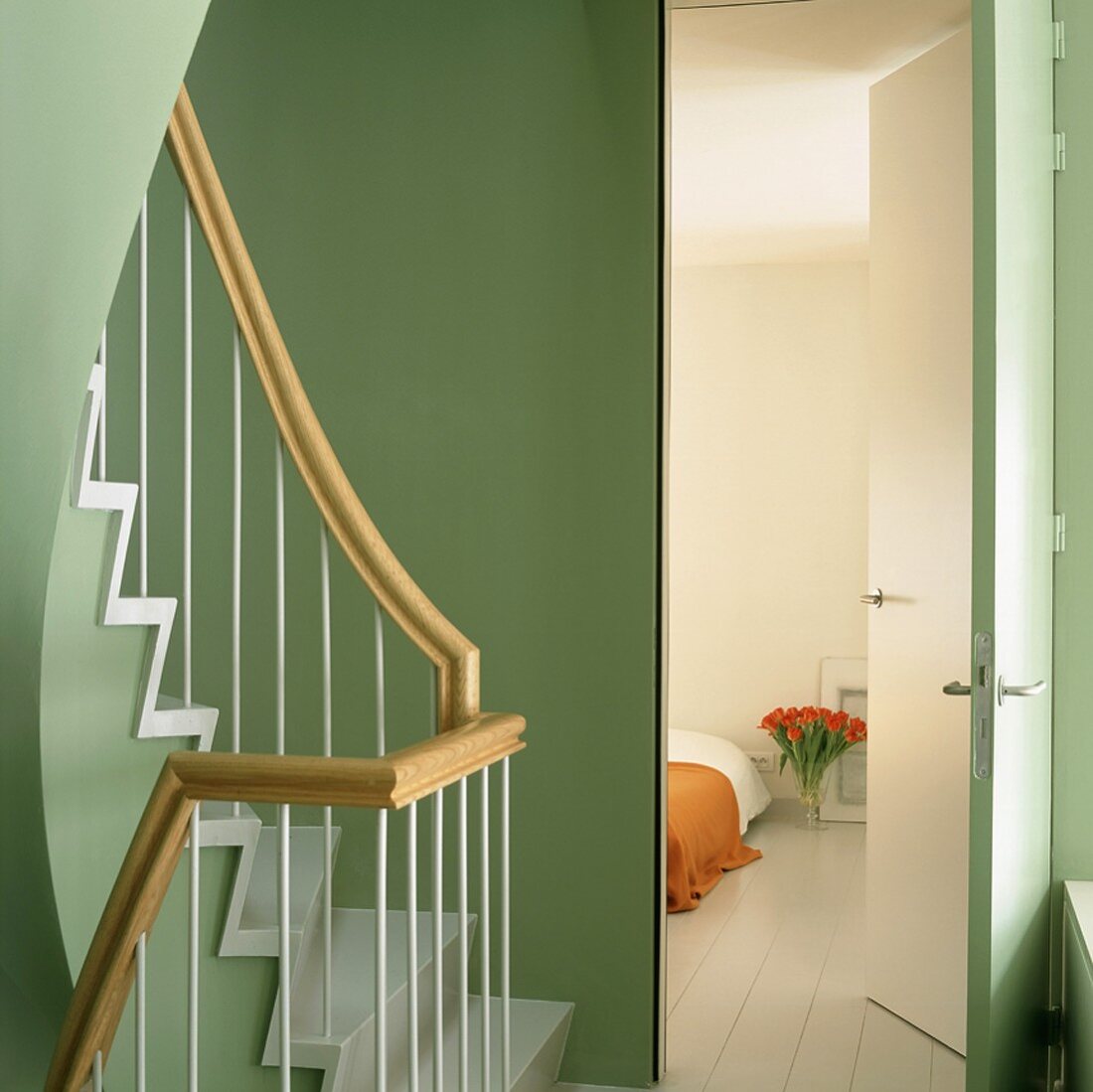 Blick vom grünen Treppenhaus in ein dezent dekoriertes Schlafzimmer