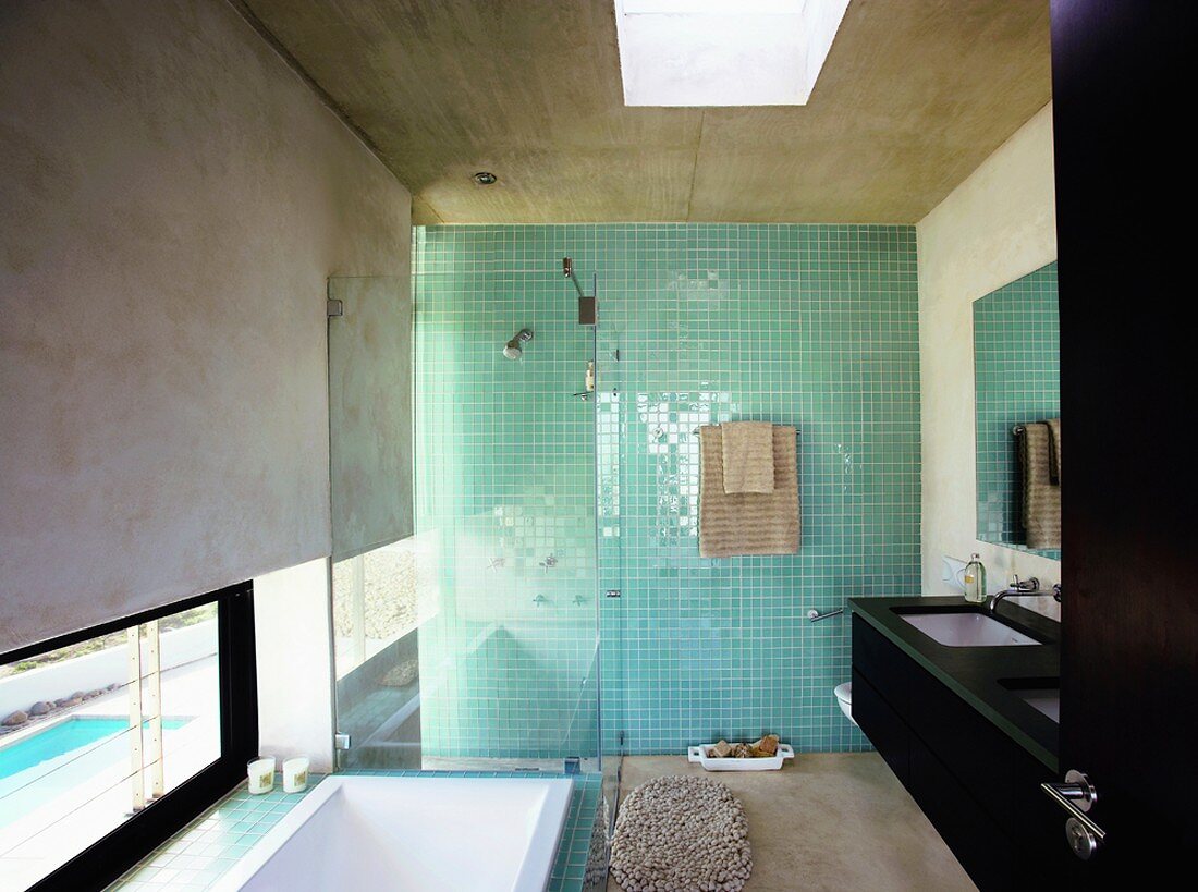 Das moderne Badezimmer mit Rohbeton an Wand und Decke fluchtet in einer mosaikbefliesten Wand in Türkis