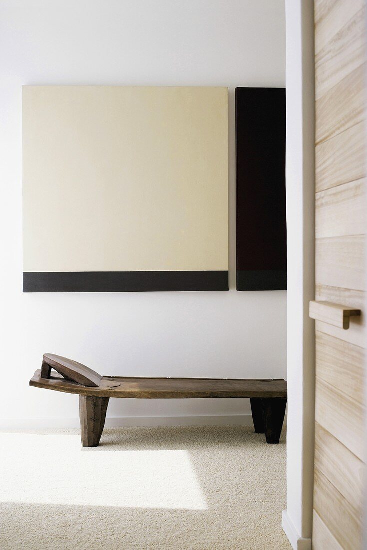 Eine schlichte, rustikale Holzliege vor einem minimalistischen Kontrastgemälde