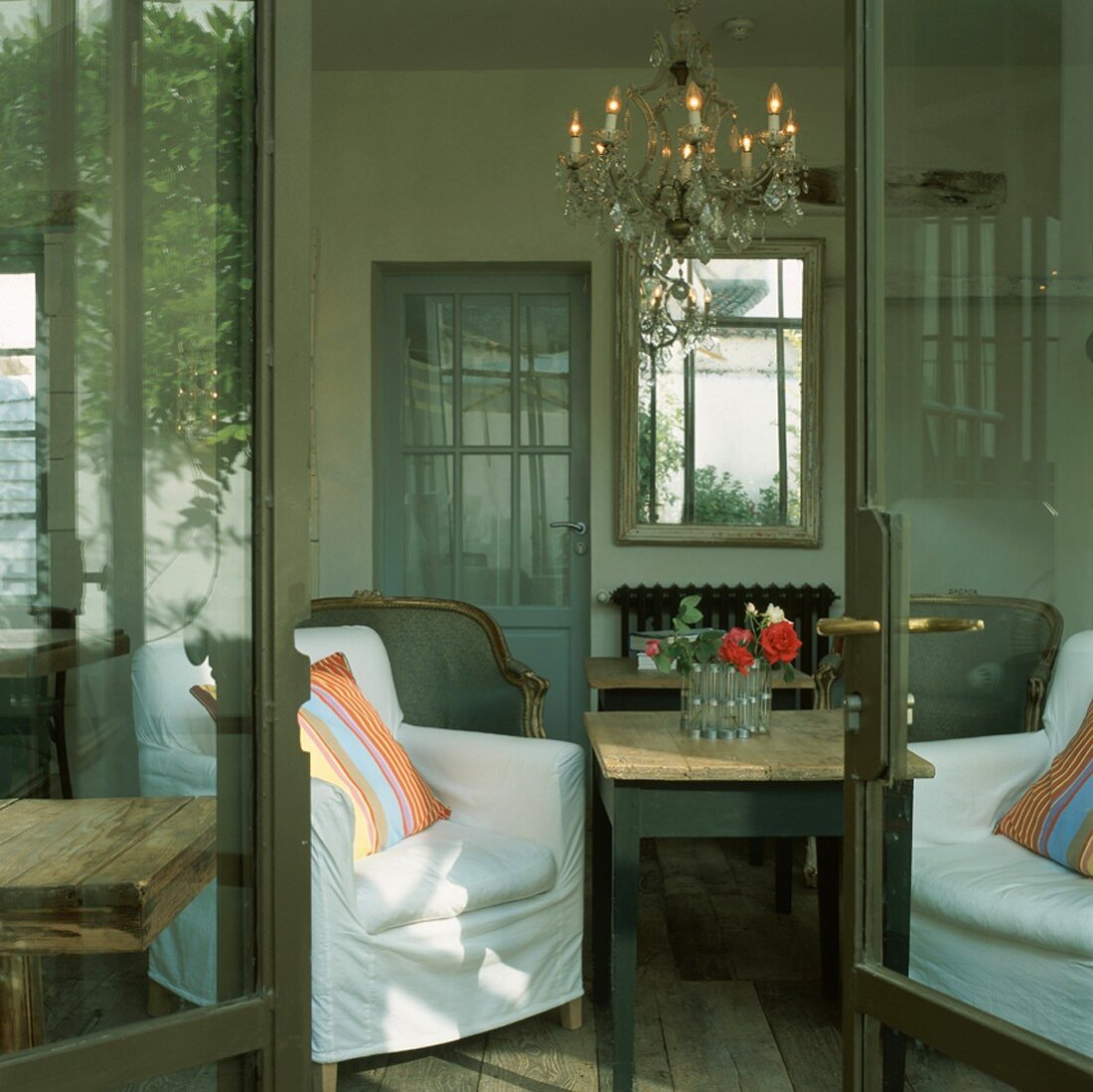 Blick durch die geöffnete Terrassentür in das Wohnzimmer mit Kronleuchter und verschiedenen Sesseln