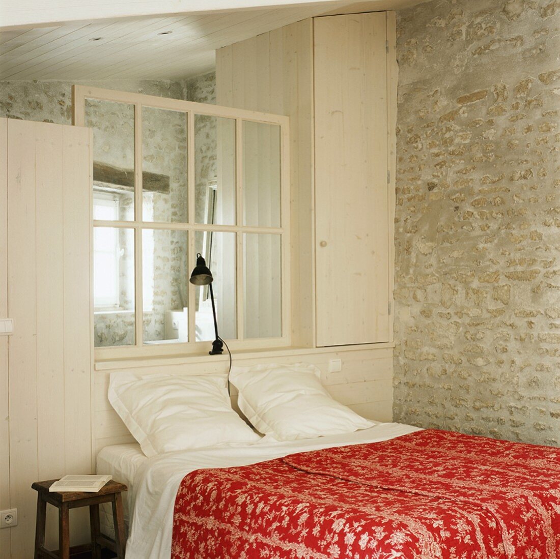 Holzeinbau mit Sprossenfenster als Kopfteil eines Doppelbettes vor einer Backsteinwand