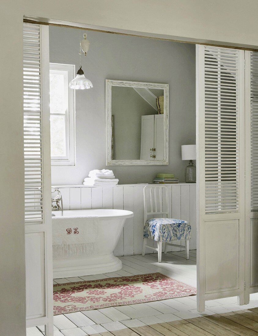 Blick durch die Jalousieschiebetür in ein romantisches Badezimmer mit Holzboden und alter Badewanne