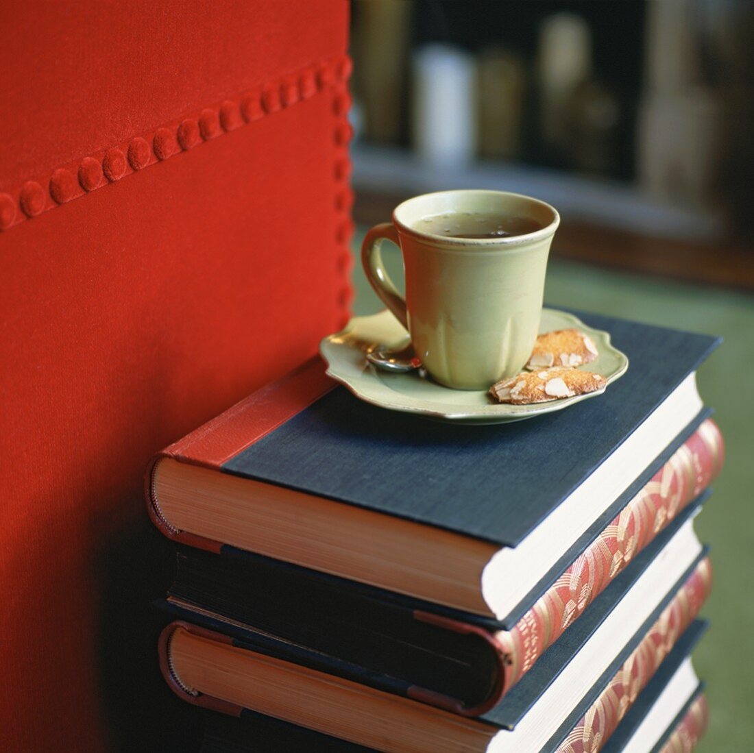 Eine grüne Teetasse mit Mandelgebäck auf einem Bücherstapel
