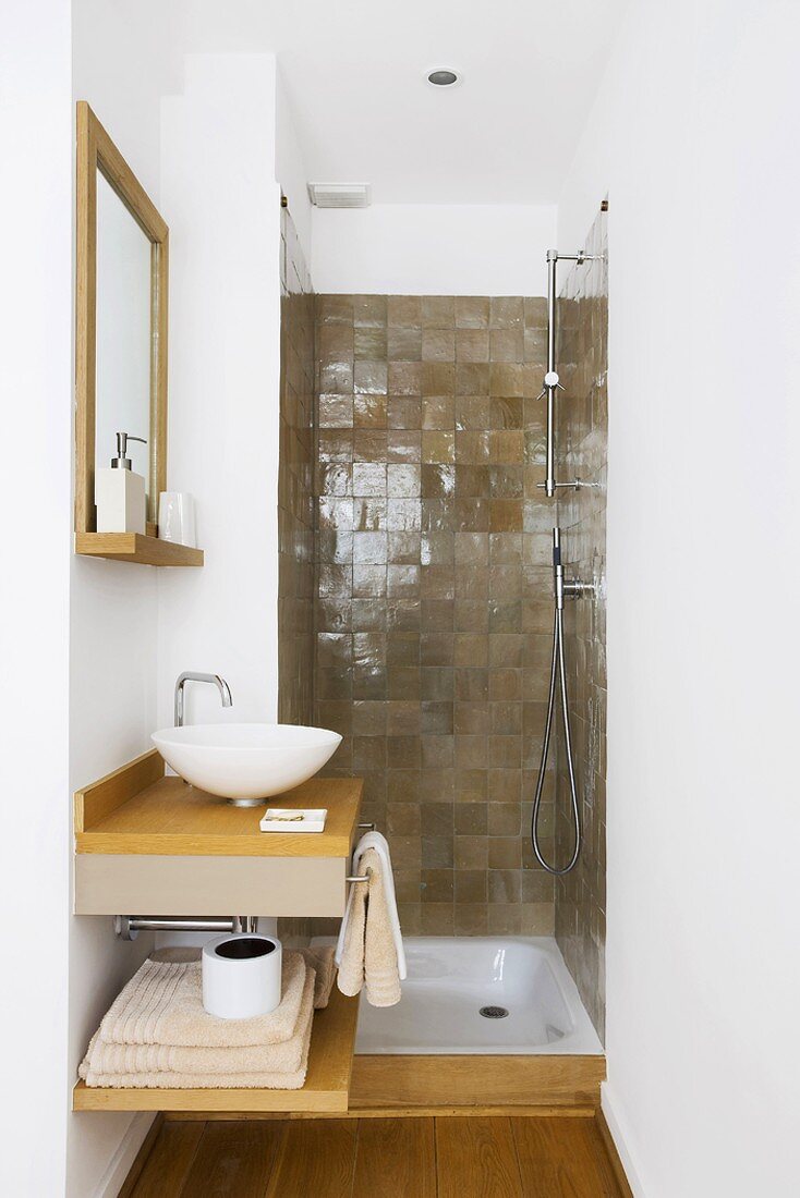 Schmales Badezimmer mit kleinem Waschtisch und braun gefliester Duschnische