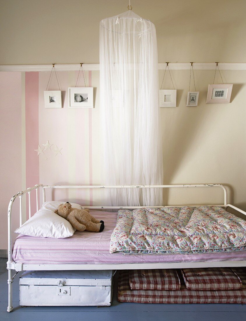 Metallbett im Shabby Chic und ein Betthimmel vor der gestreiften, dekorierten Wand eines Kinderzimmers