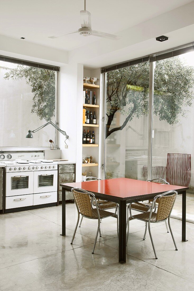 Bunter Esstisch und Metallstühle in einer hellen Küche mit großem Fenster und Terrassentür