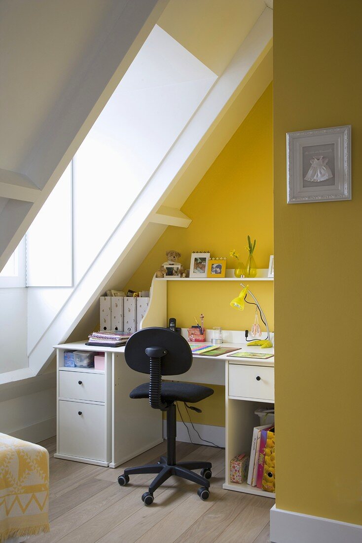 Kleine Arbeitsecke im gelben Dachgeschosszimmer mit großem Dachfenster