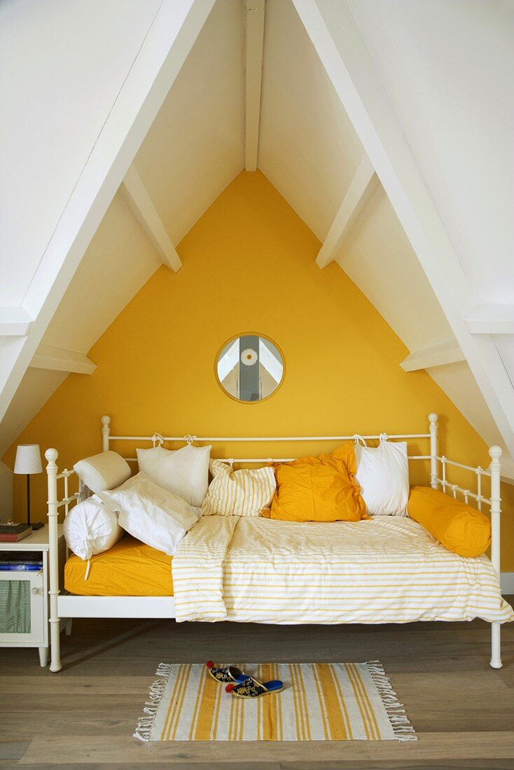 Weisses Metalltagesbett in der gelb gestrichenen Gaube des Dachgeschosses