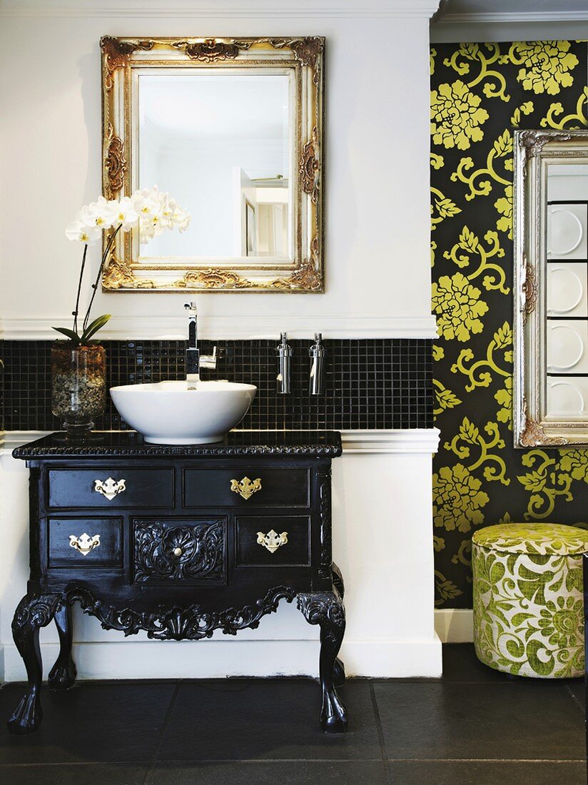 Eine schwarz lackierte Barockkommode dient mit einem modernen Becken als Waschtisch und wird stilistisch durch einen goldenen Spiegel ergänzt