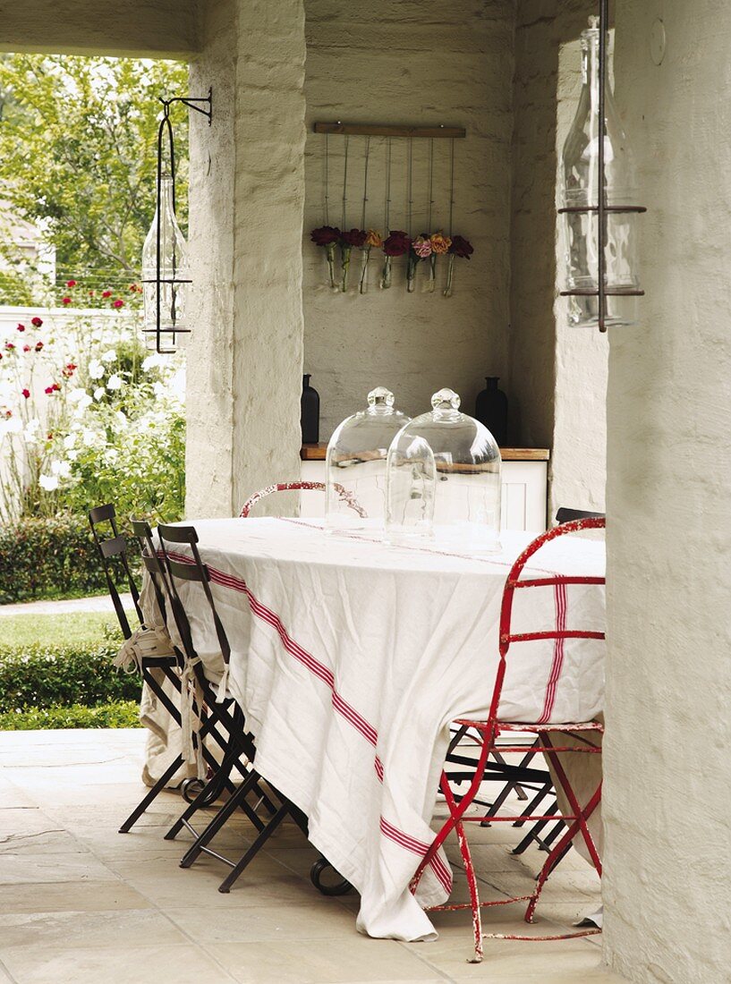 Gartentisch mit zwei Glasglocken auf der überdachten Steinterrasse mit kleiner Schranknische