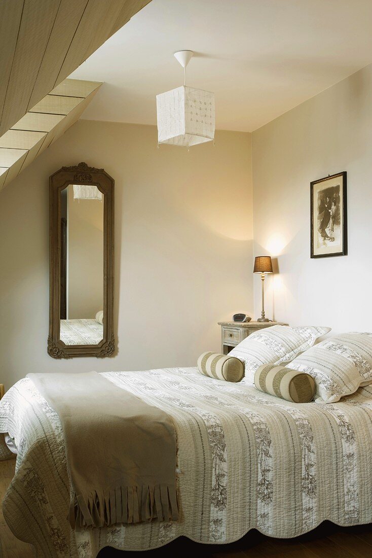 Nackenrollen und Zierkissen auf der Tagesdecke eines Doppelbettes im Schlafzimmer mit Gaubenfenster