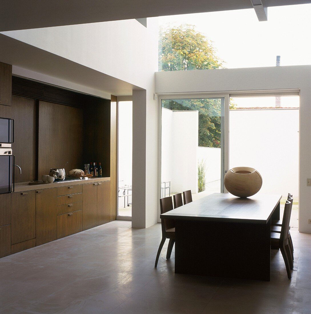 Minimalistische Küche mit Esstisch vor einer verglasten Terrassenfront in moderner Architektur