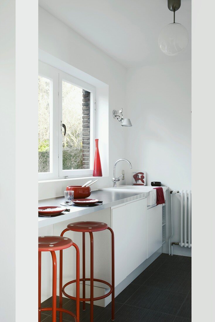 Rote Barhocker an einer weissen Küchenzeile mit Edelstahloberfläche