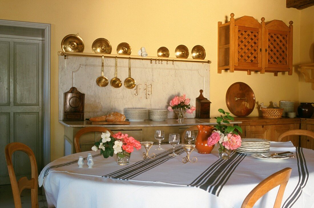 Eine Sammlung von Topfdeckeln und Schöpfkellen aus Messing in einer Landhausküche mit gedecktem Esstisch