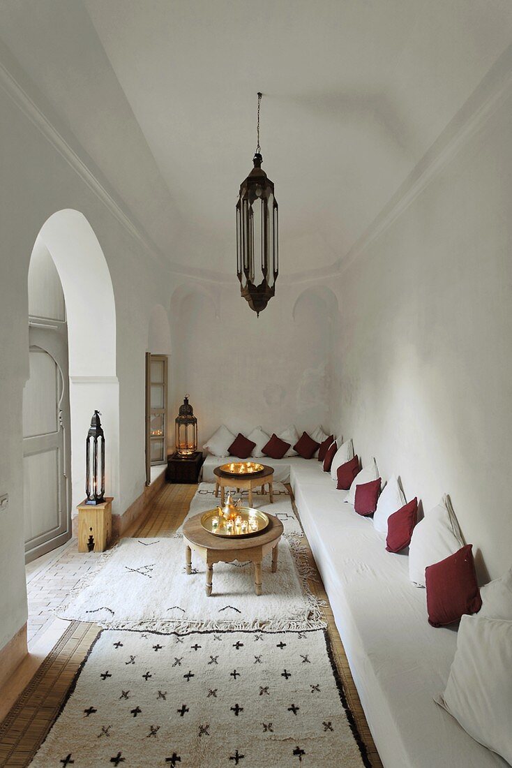 Weisser Wohnraum im marokkanischen Stil mit langer Polsterbank und vielen Teppichen