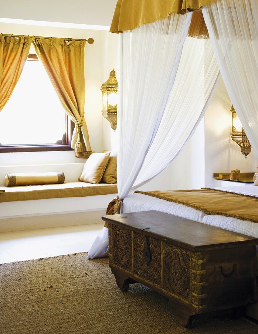 Ein Schlafraum im orientalischen Stil mit Himmelbett, antiker Holztruhe und gepolsterter Sitzbank am Fenster