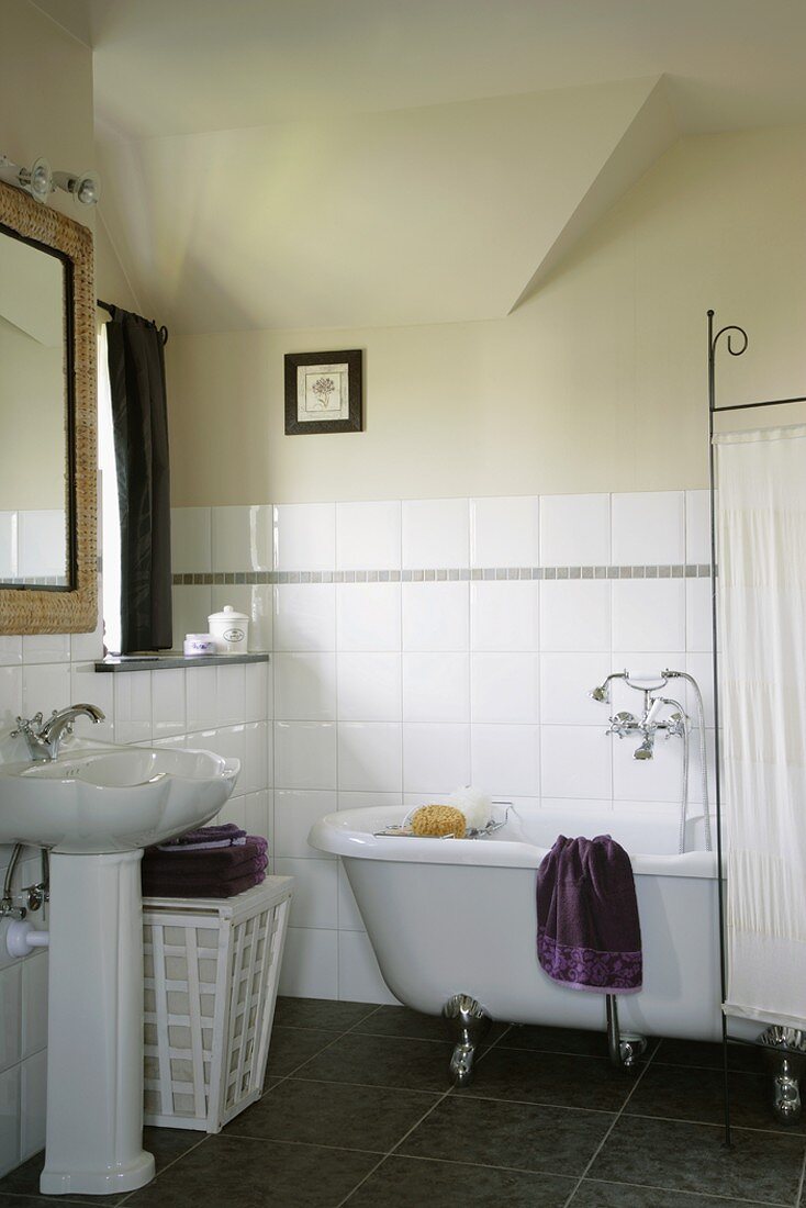 Dekoratives Waschbecken und freistehende Antikbadewanne in einem klassischen Badezimmer mit halbgefliester Wand und schwarzen Bodenfliesen