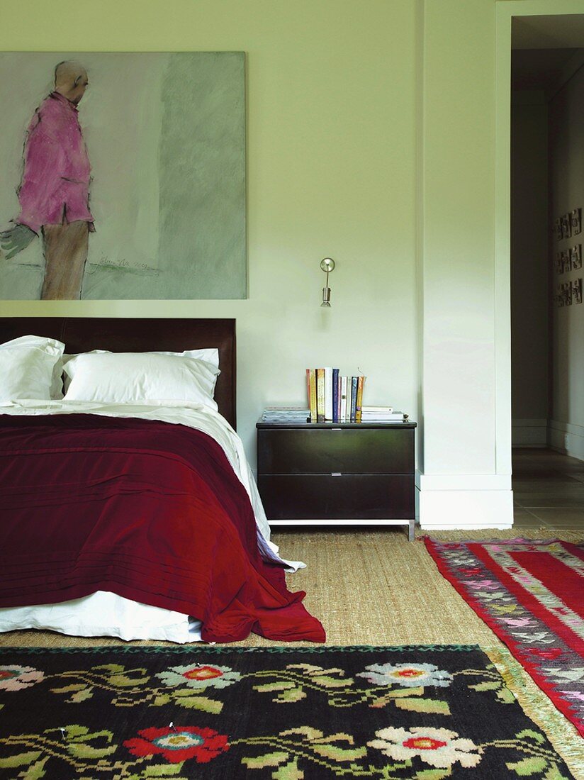 Bunter Teppichmix im Schlafzimmer mit elegantem Bett und Nachtschränkchen unter einem Gemälde