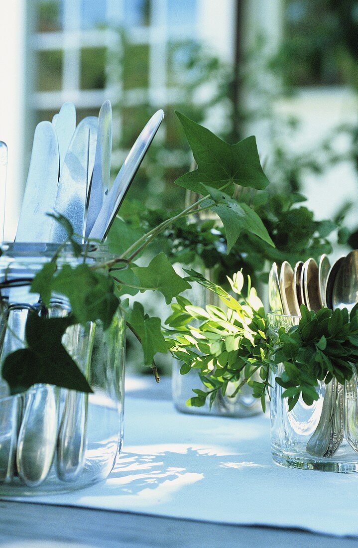 Garden party: cutlery in glasses decorated with greenery