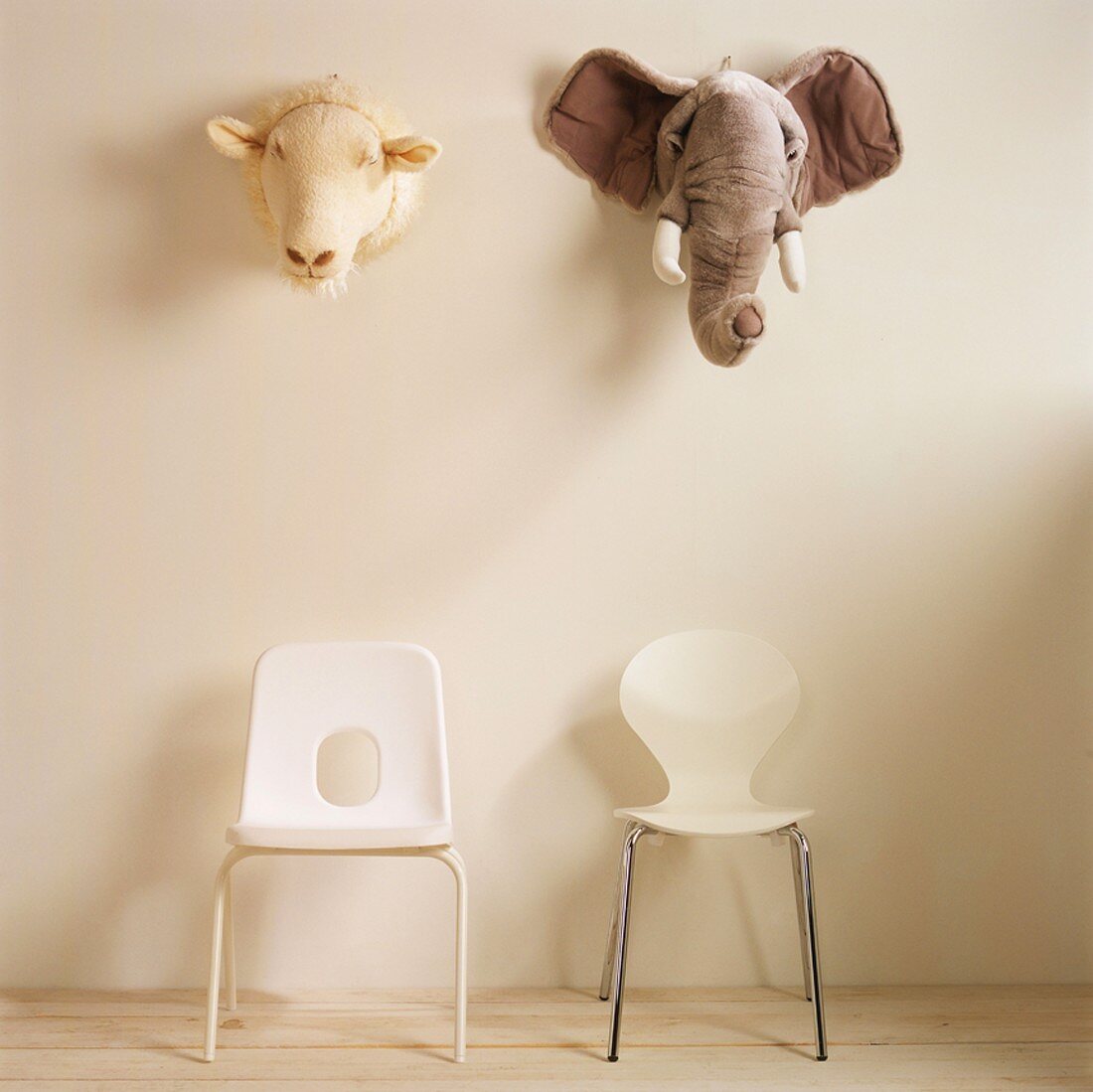 Schaf- und Elefantenkopf aus Plüsch über zwei Kinderstühlen an der Wand hängend