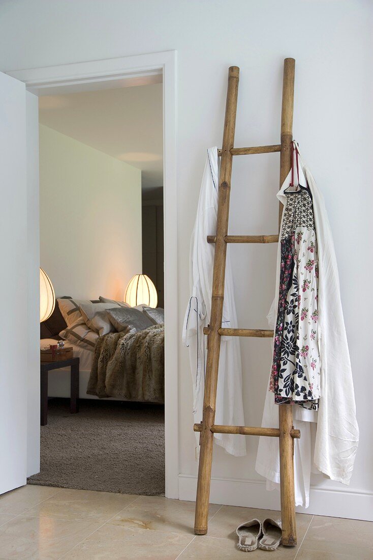 Blick vom Vorraum mit Holzgarderobe in Form einer Leiter durch die geöffnete Tür ins Schlafzimmer