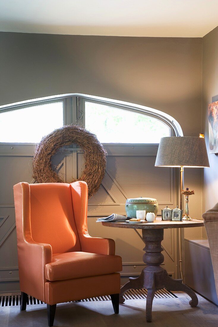 Sitzecke mit orangefarbenem Sessel und rundem Tisch in Raum mit großem Tor und Fensterschlitz