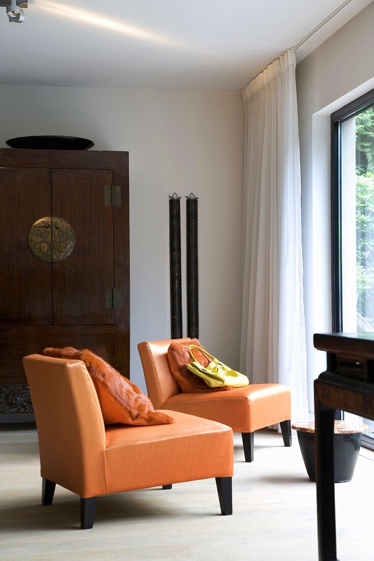 Modernes Wohnzimmer mit großer Fensterfront und davor platzierten Ledersesseln mit Fellkissen im selben Farbton