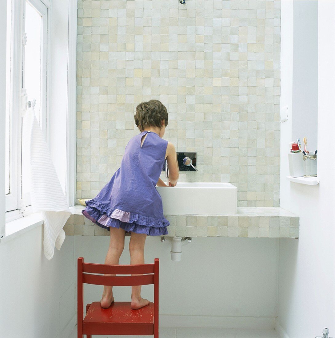 Kind auf einem Stuhl stehend beim Händewaschen
