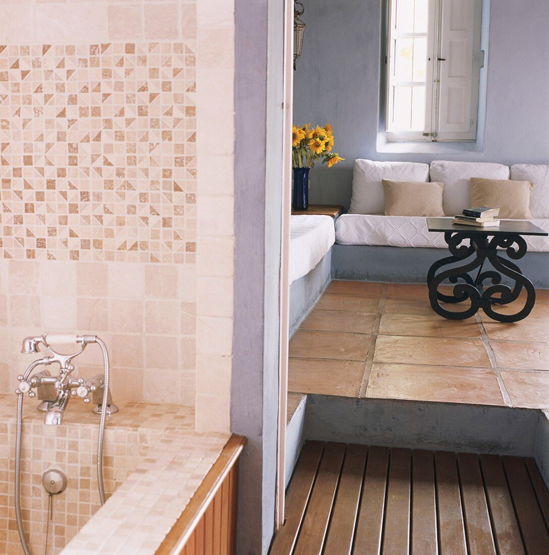 Blick vom Badezimmer in abgedunkeltes Wohnzimmer mit weissen Sitzpolstern und Terrakottafliesen