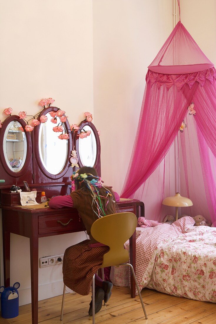 Mädchen sitzt an Schminktisch in Kinderzimmer mit rosafarbenem Himmelbett